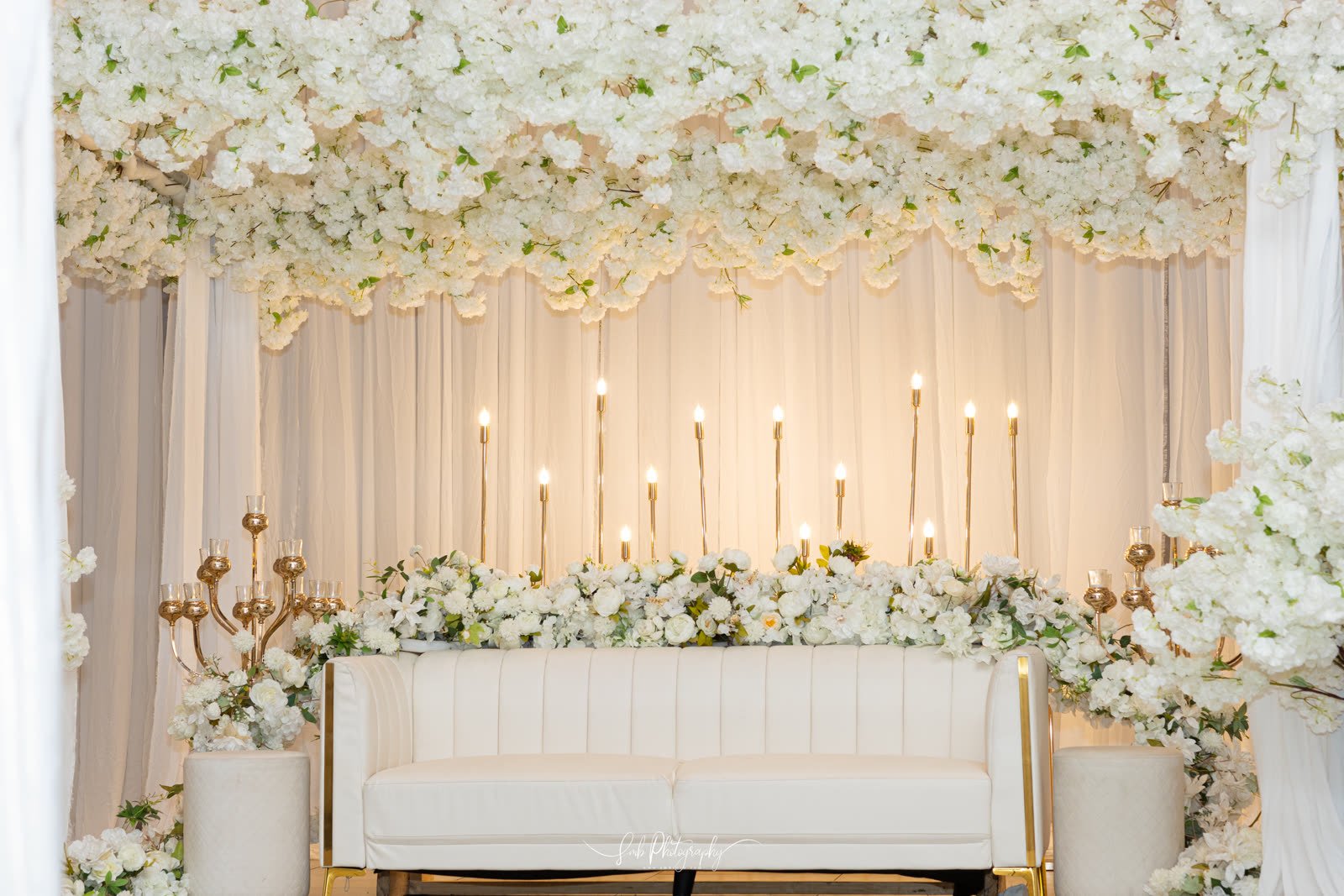 A white flower wall behind the couple's seat