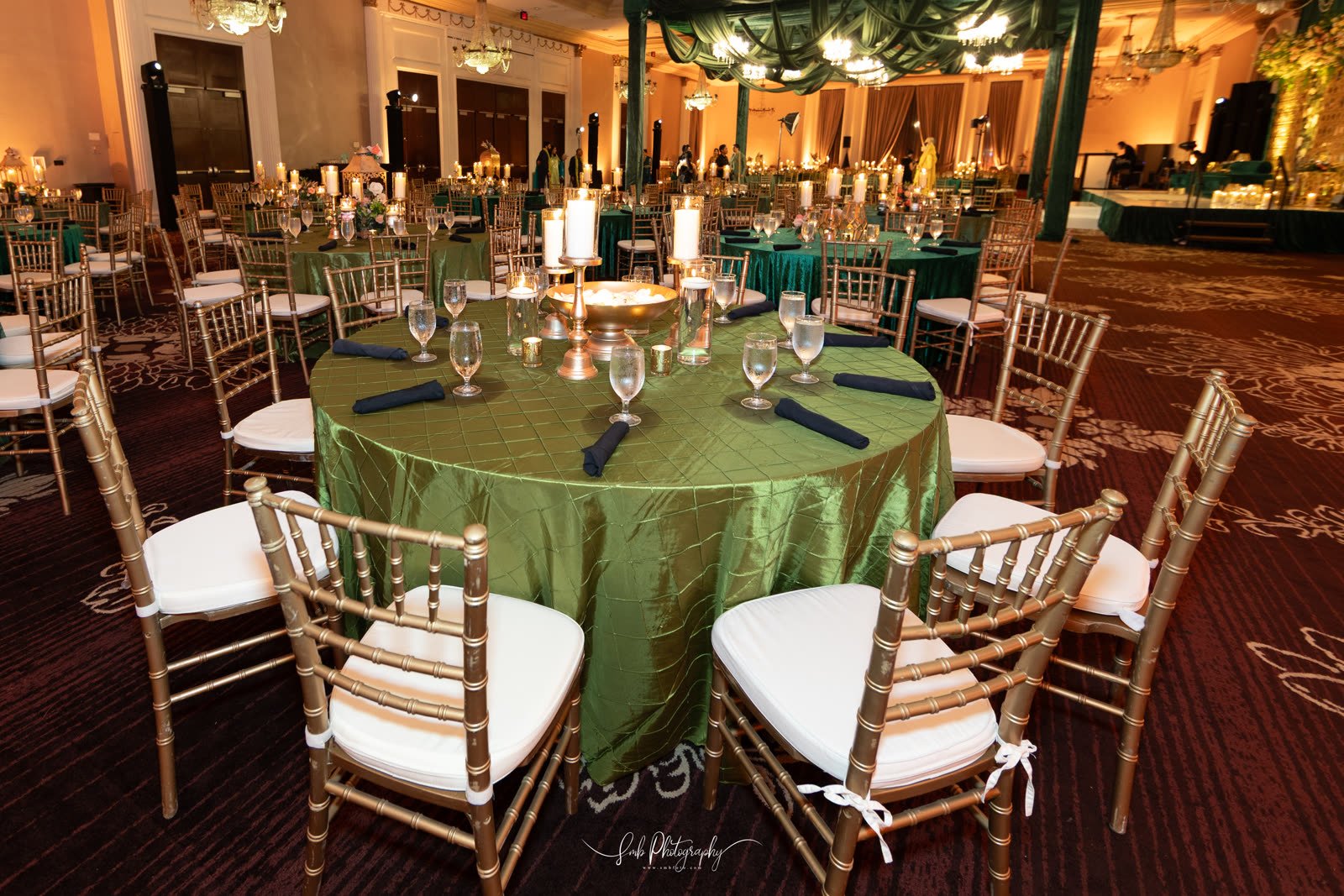 A green-linened table set with glassware and gold chairs