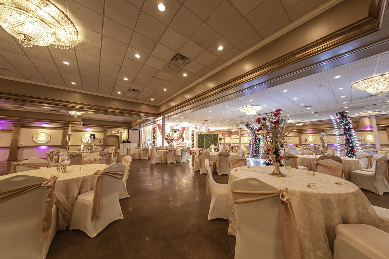 The room set with round tables, a floral arch at the head of the floor